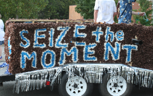   A side view of a homecoming float with the "Seize the Moment" slogan in paper flowers.
